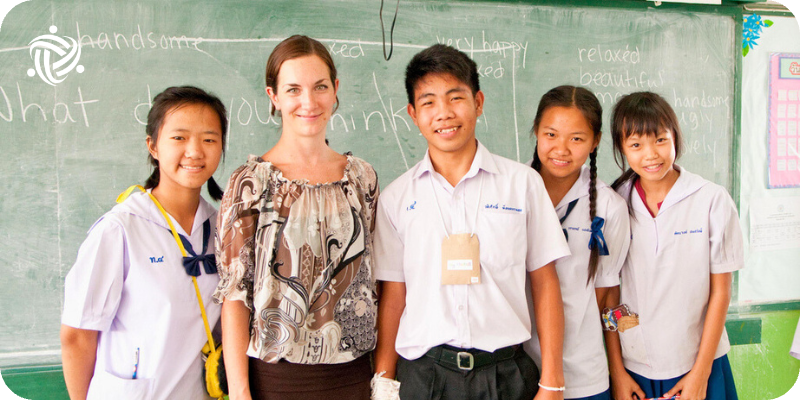 A Teaching Volunteer stand in front of a blackboard in Thailand.