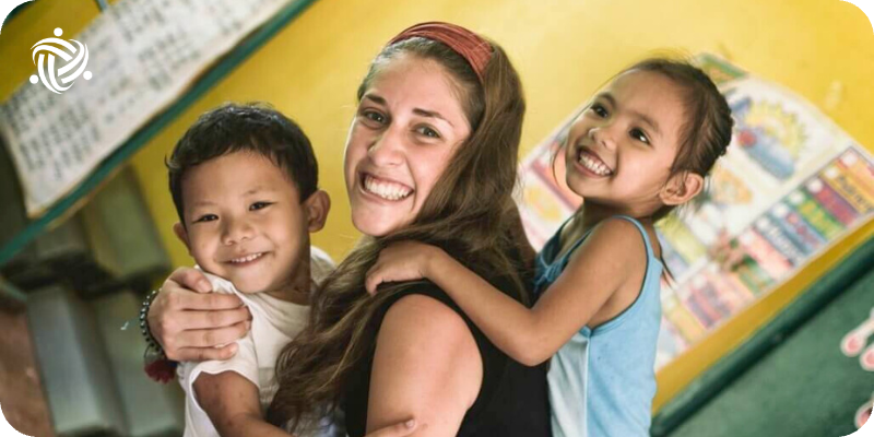 A Woman Volunteering with children in Philippines with two of them in her arms.